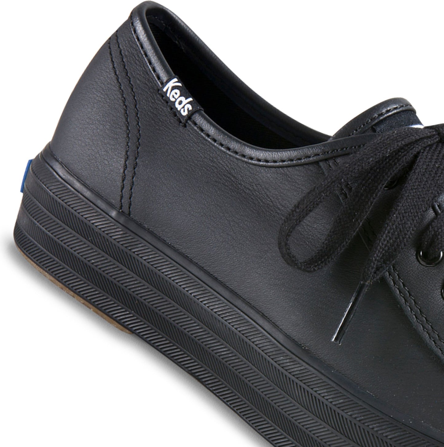 Close-up of a black sneaker with black laces and a thick, black, ribbed sole. The word "Keds" is stitched on the back.