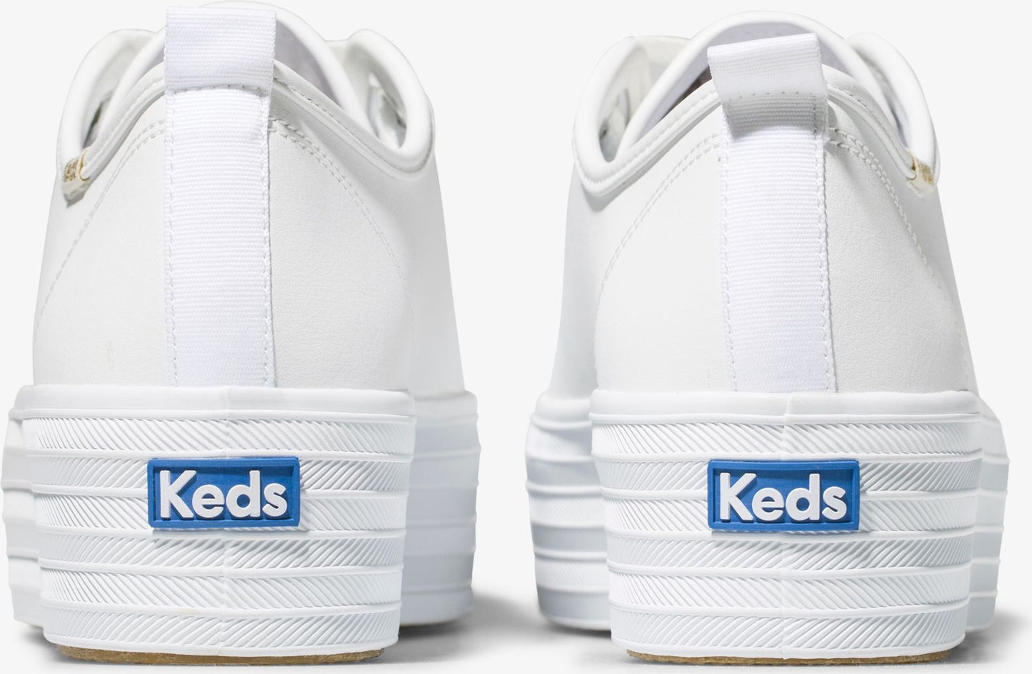 White platform sneakers with 'Keds' in blue on the back of each.