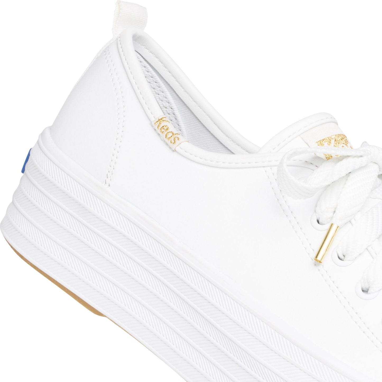 Close-up of a white leather sneaker with white laces and a thick striped white rubber sole. The brand name "Keds" is printed inside.