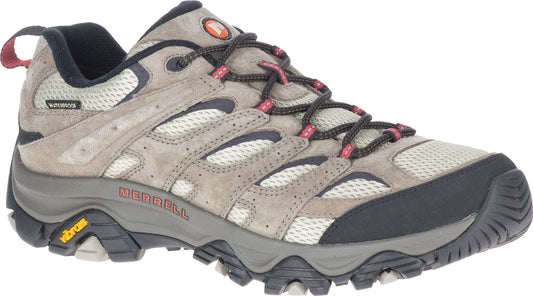 A low-cut hiking shoe features beige suede and mesh, a dark grey toe cap and sole, black laces with pink accents, a red pull tab, and the word 'MERRELL' in red near the heel.