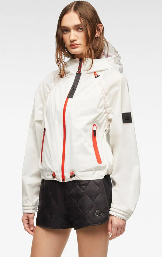 A woman wears a white long-sleeve windbreaker jacket with orange trim and black accents, and black quilted shorts.