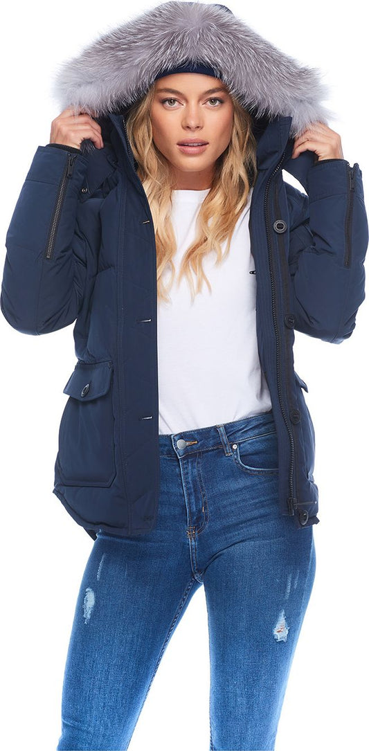 A woman wearing a blue parka with a fur-trimmed hood and blue jeans.