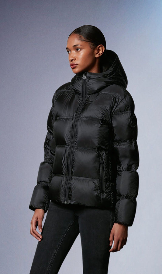 A woman poses wearing a black, puffy down jacket with a hood, paired with black pants.