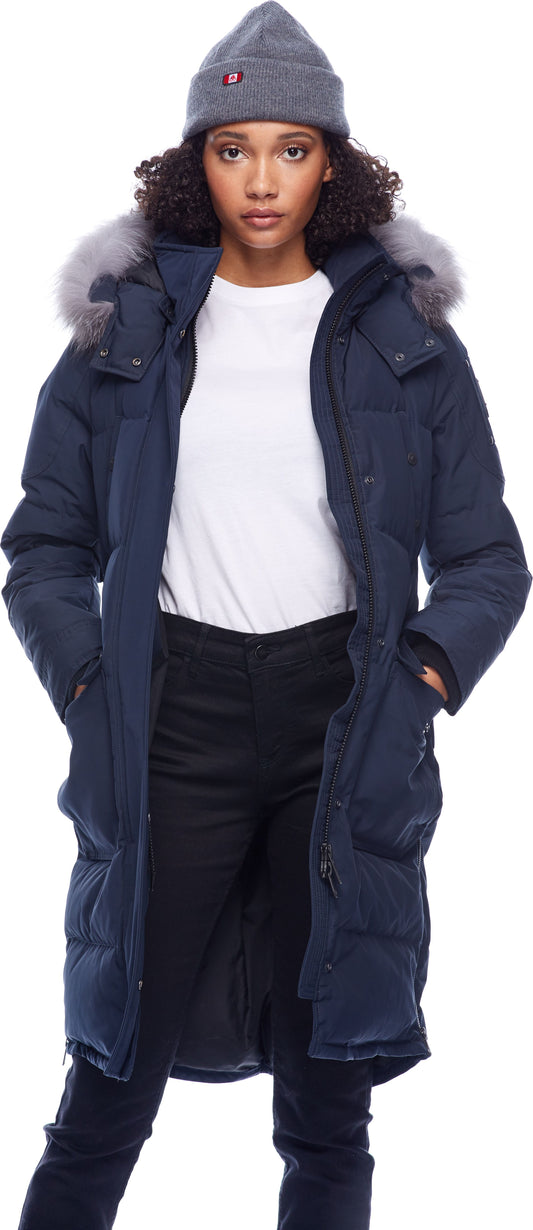 A woman wearing a gray beanie, white shirt and a long, navy blue parka with fur trim on the hood.
