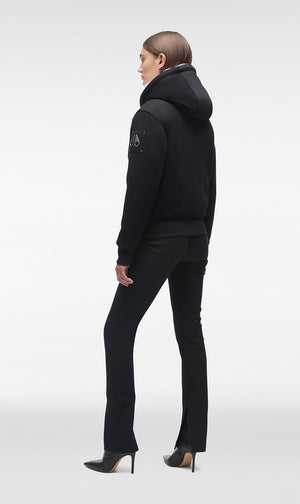 Woman wearing a black hooded jacket and black slacks.