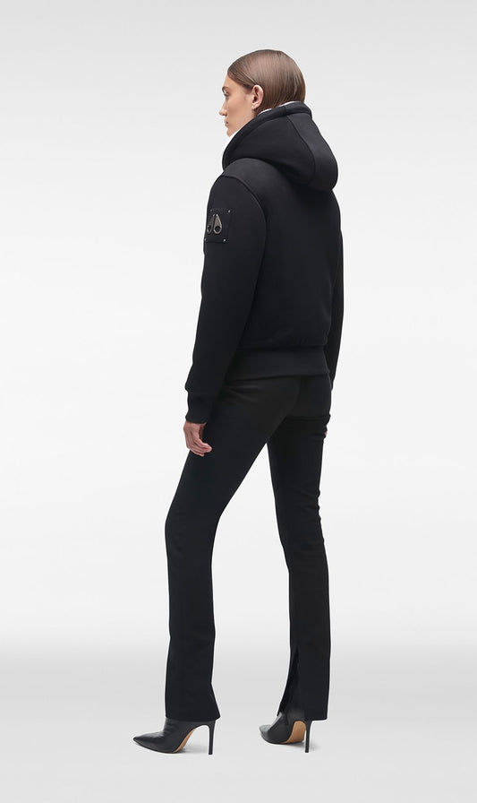 Woman wearing a black hooded jacket and black slacks.