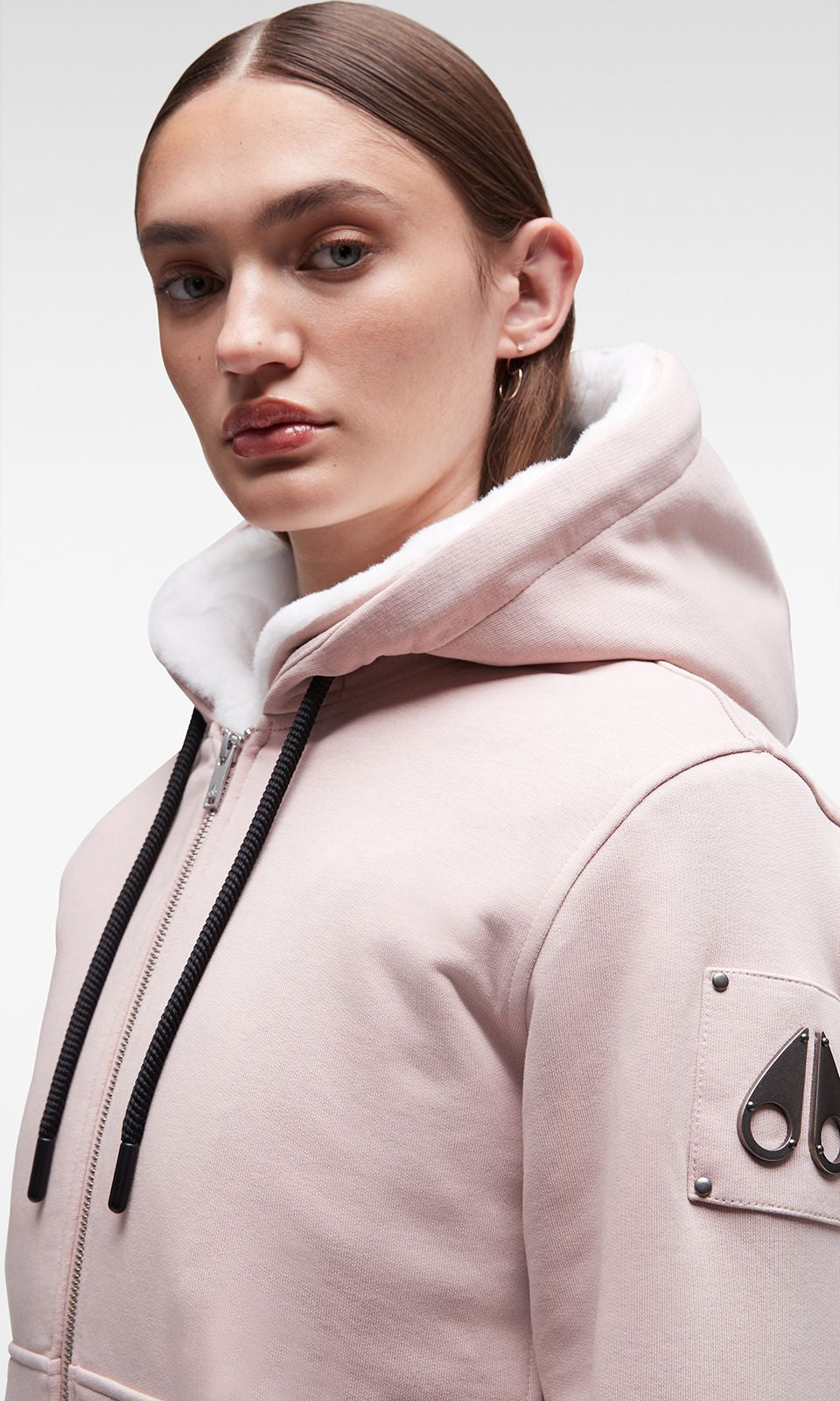 A person wearing a pink hooded sweatshirt with a zipper and a logo on the sleeve.