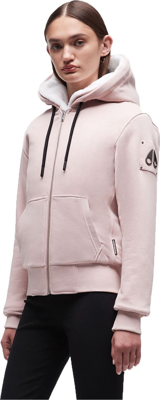A woman wearing a light pink hooded zip-up sweatshirt with a white lining and black drawstrings.