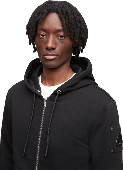 Black hoodie with zipper and logo emblem on sleeve, worn by a model.