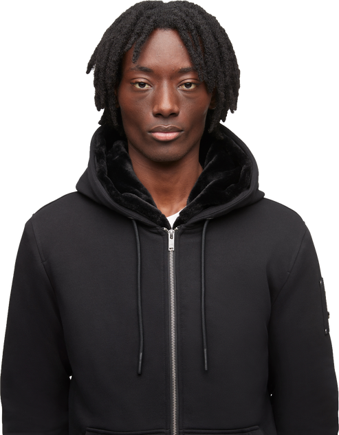 A man in a black hooded zipper sweatshirt with a furry black lining around the hood.