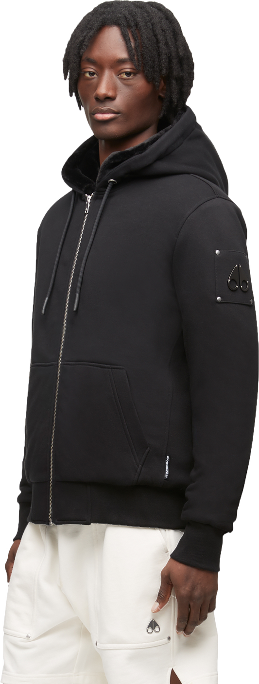 A person wearing a black zip-up hooded sweatshirt and white shorts.