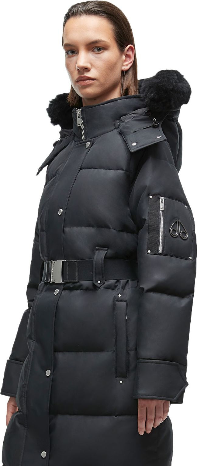 A person wearing a long, black puffer coat with a belted waist and a hood lined with fur.