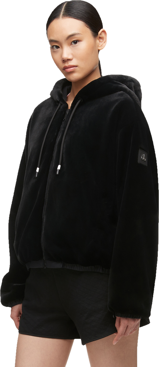 A person wearing a black fuzzy hooded jacket and black shorts.