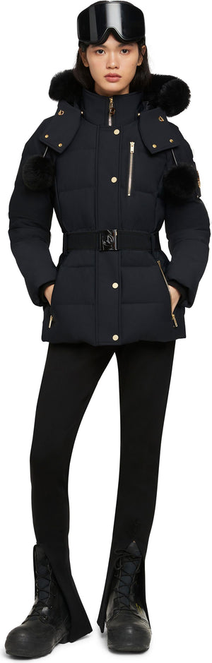 A woman wearing a black ski jacket, black leggings, and black snow boots, also wearing ski goggles on her head.