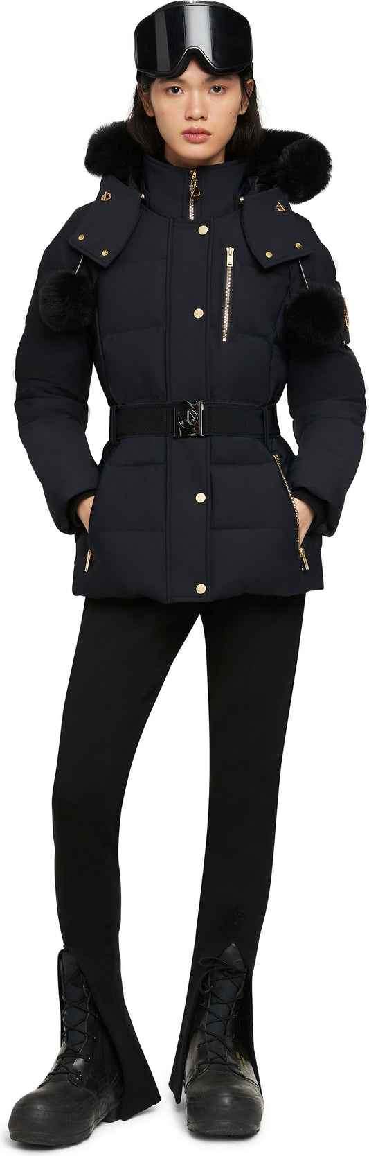 A woman wearing a black ski jacket, black leggings, and black snow boots, also wearing ski goggles on her head.
