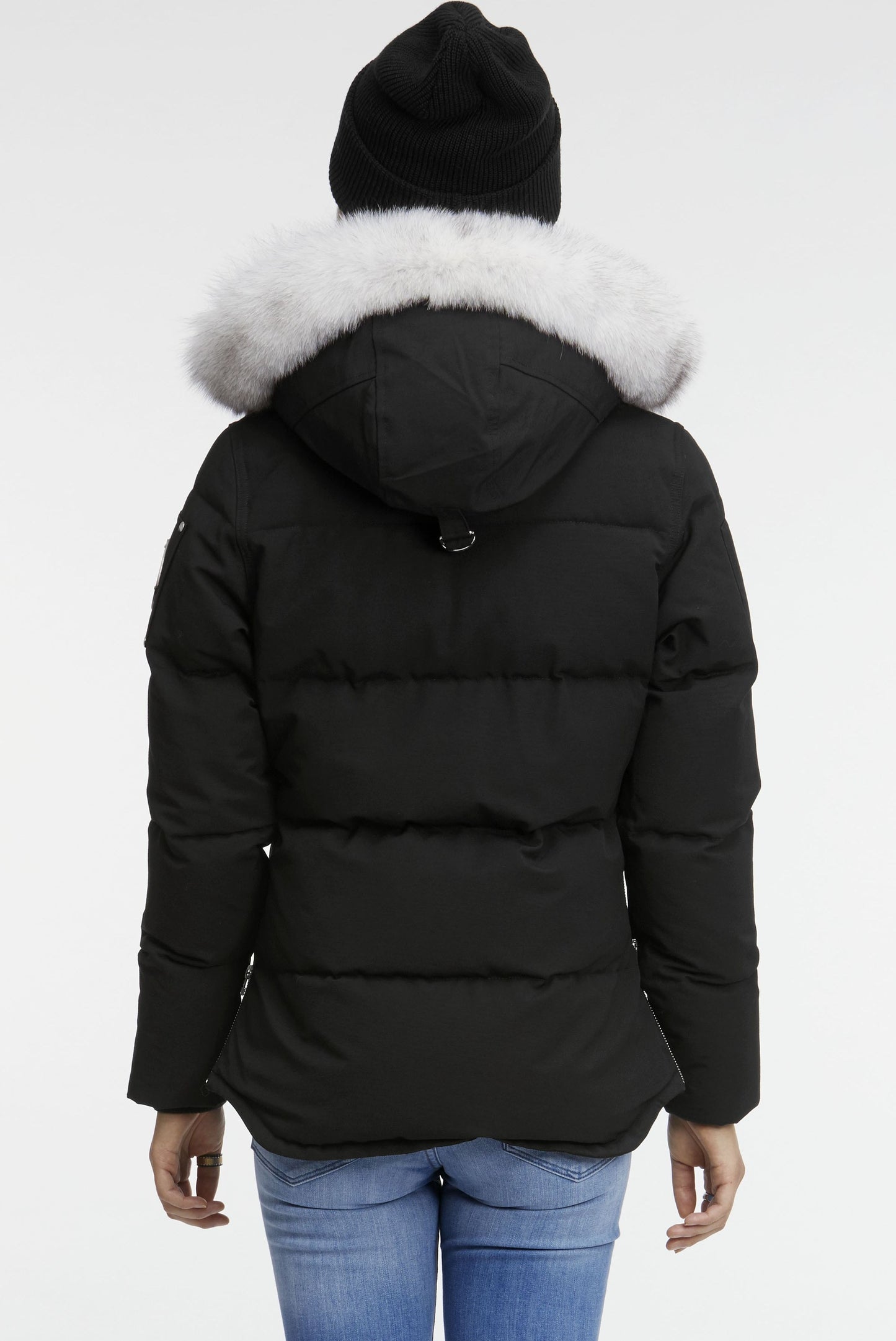 Back view of a black down puffer jacket with a white fur-trimmed hood and a person in a black knit hat.