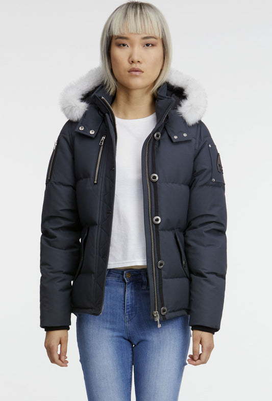 A woman is wearing a dark blue puffer jacket with a white fur-lined hood and blue jeans.