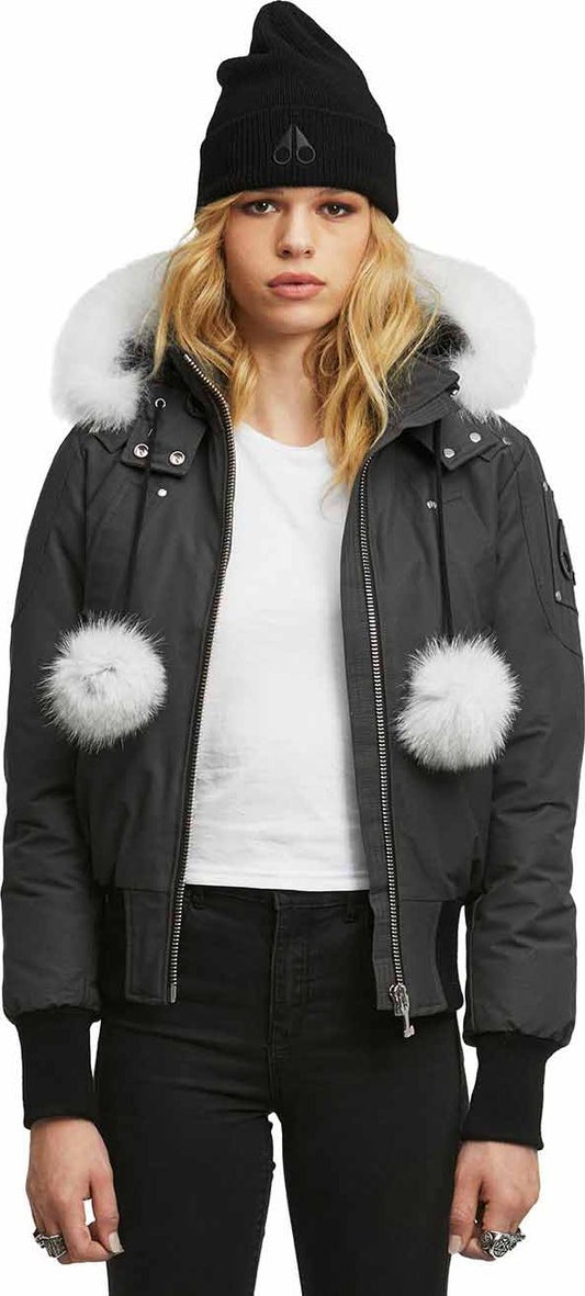 A person wearing a black beanie and a gray bomber jacket with a white fur-lined hood and white pom-poms.