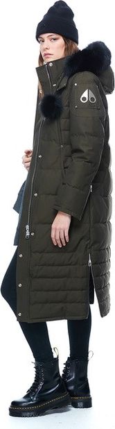 A person wearing a dark green long winter coat, a black beanie, black leggings and shiny black combat boots.