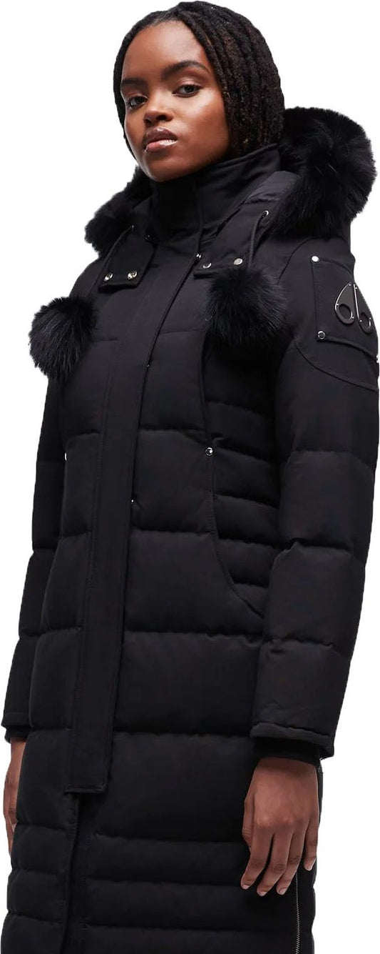 A person wears a long black quilted coat with fur trim on the hood and pockets.