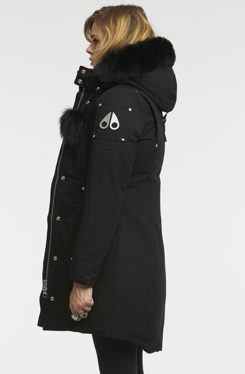 Side view of a person wearing a black down parka with a fur-trimmed hood and silver logo on the sleeve.