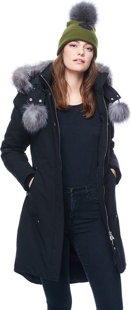 A woman in a black winter coat with fur trim and a green beanie with a pom-pom.