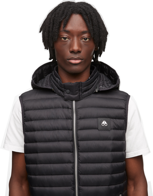 A man wearing a black puffer vest with a hood and a small logo.