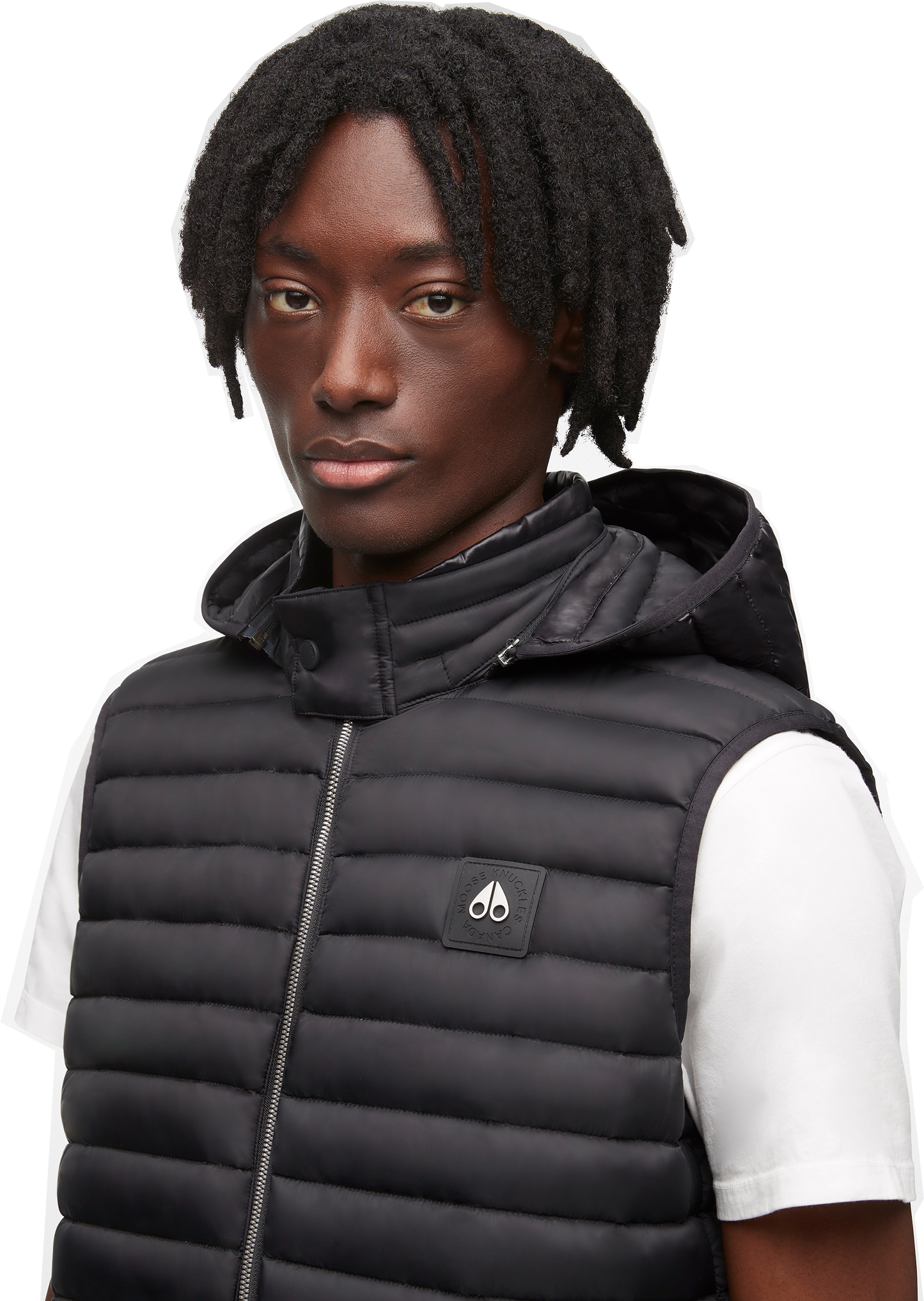 A dark-skinned person with dreadlocks wearing a black puffer vest over a white t-shirt.