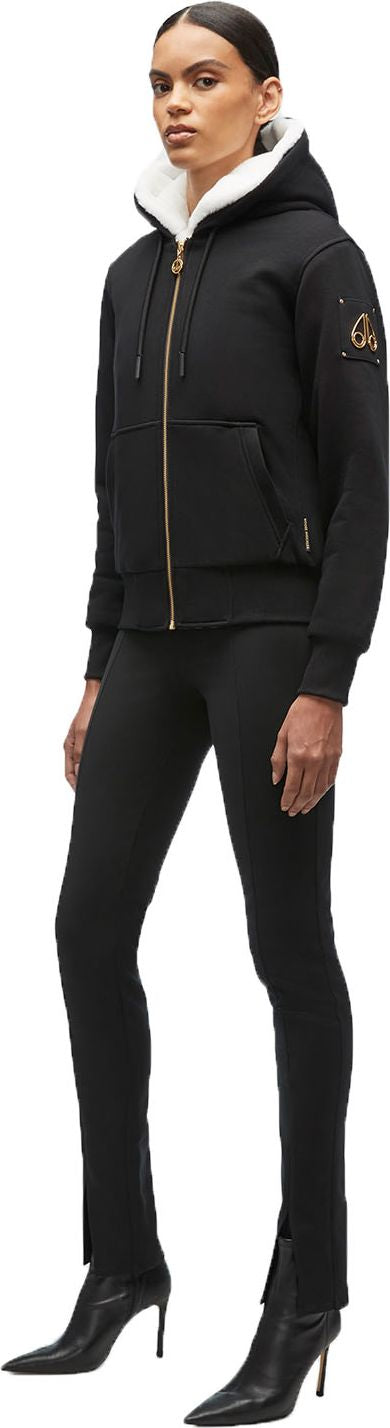 A person wearing a black hooded jacket with white fur lining, black leggings, and heeled boots.