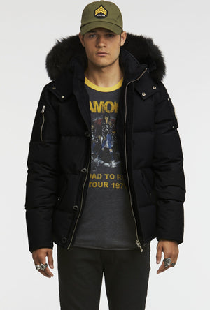 A person wearing a black winter jacket with a fur-lined hood and a green baseball cap.