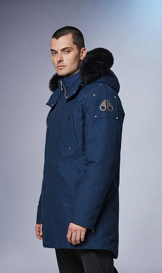 Man wearing a blue parka with fur hood and metal logos on the upper arm.