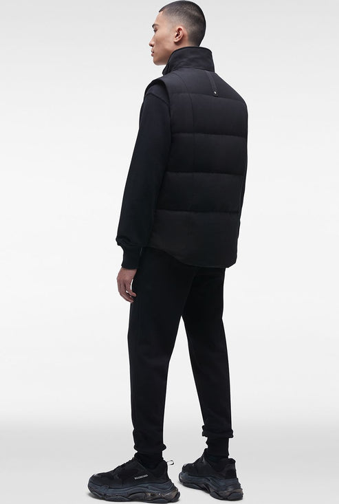 A person wearing a black puffer vest, black sweater, black pants, and black sneakers.