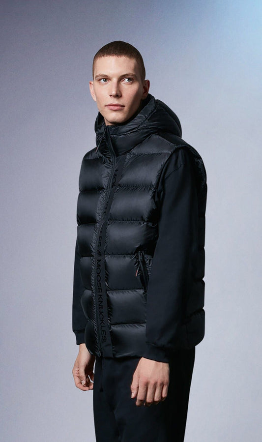 A man wearing a black hooded down vest with a black long sleeve shirt and pants.