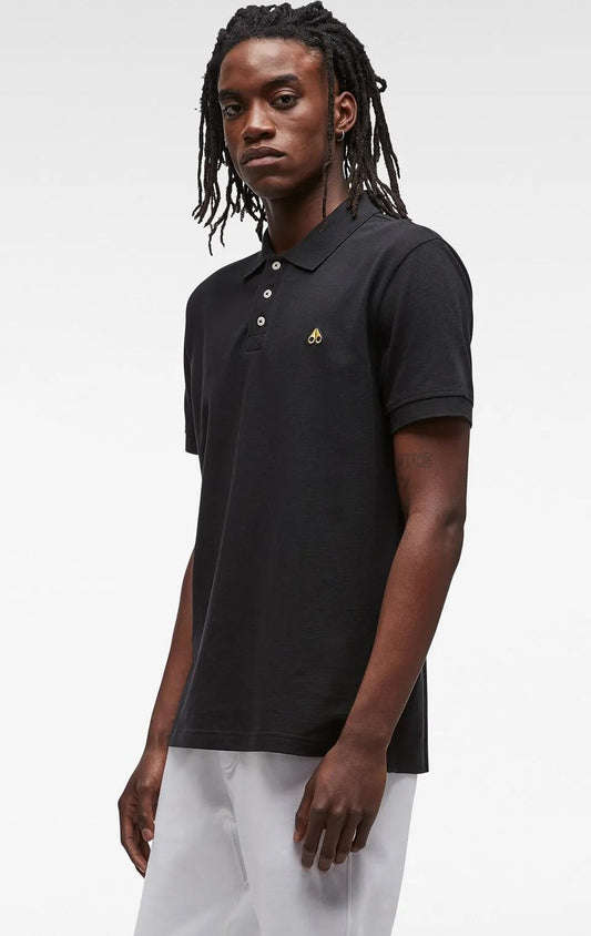 Man wearing black polo shirt with a small gold logo on the chest and white pants.