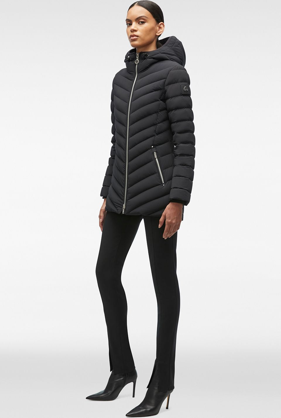 A woman wearing a black puffer coat, black pants and black heels.