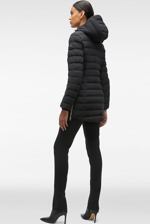 A woman is standing, wearing a black puffy coat with a hood and black pants with black heels.