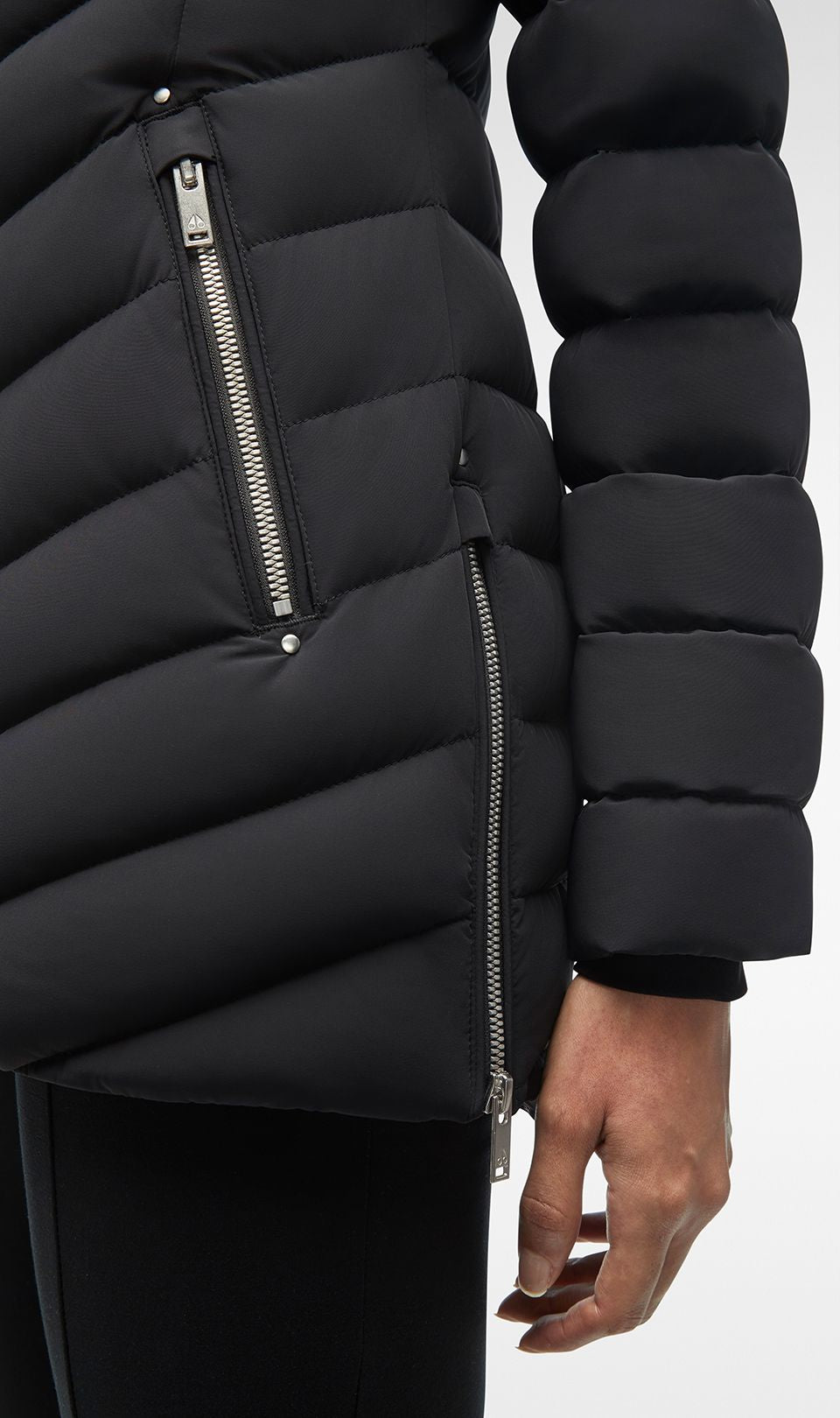 Close-up of a black puffer jacket with silver zippers on the side and arm.