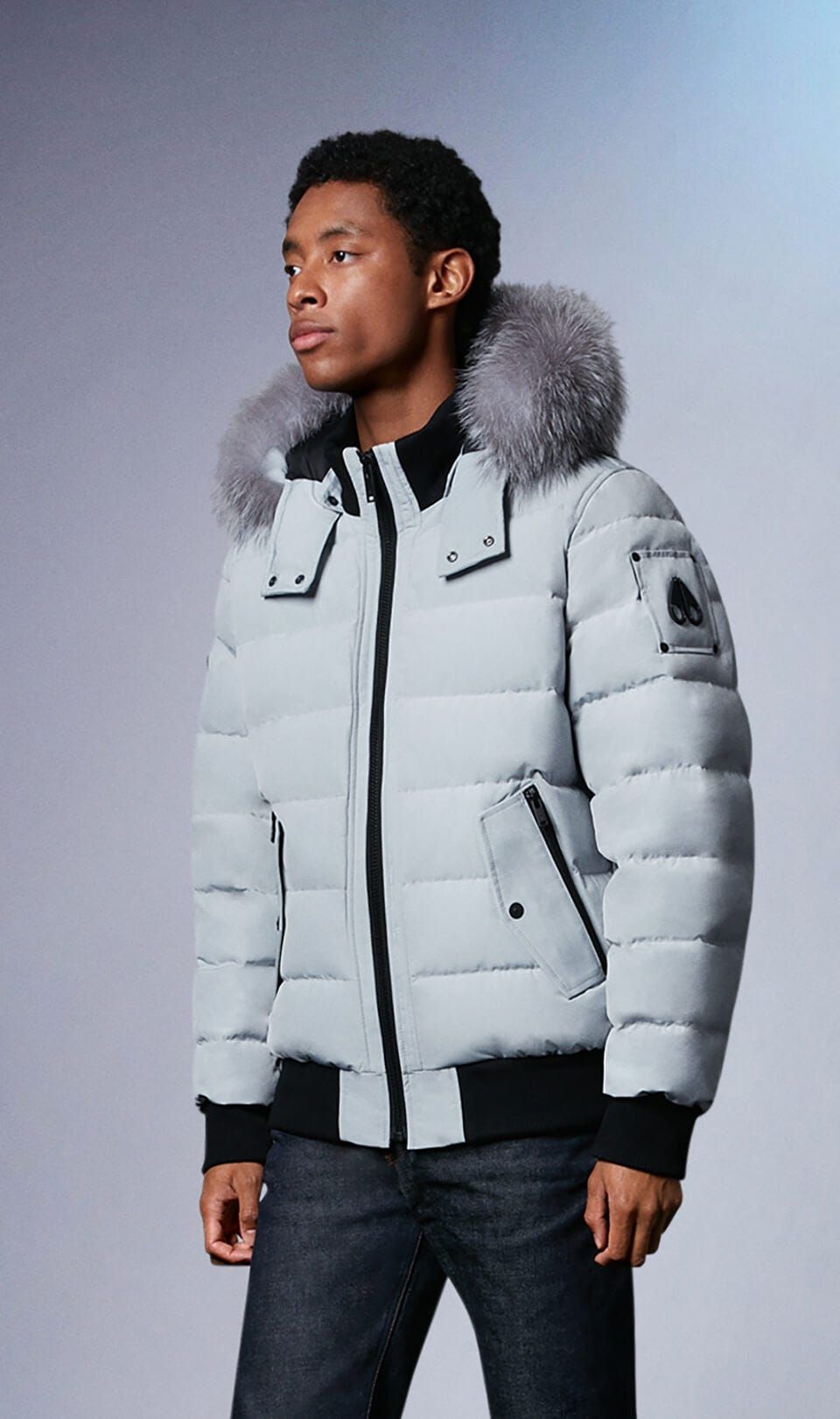 A person wearing a light blue puffer jacket with a fur-trimmed hood and black trim.