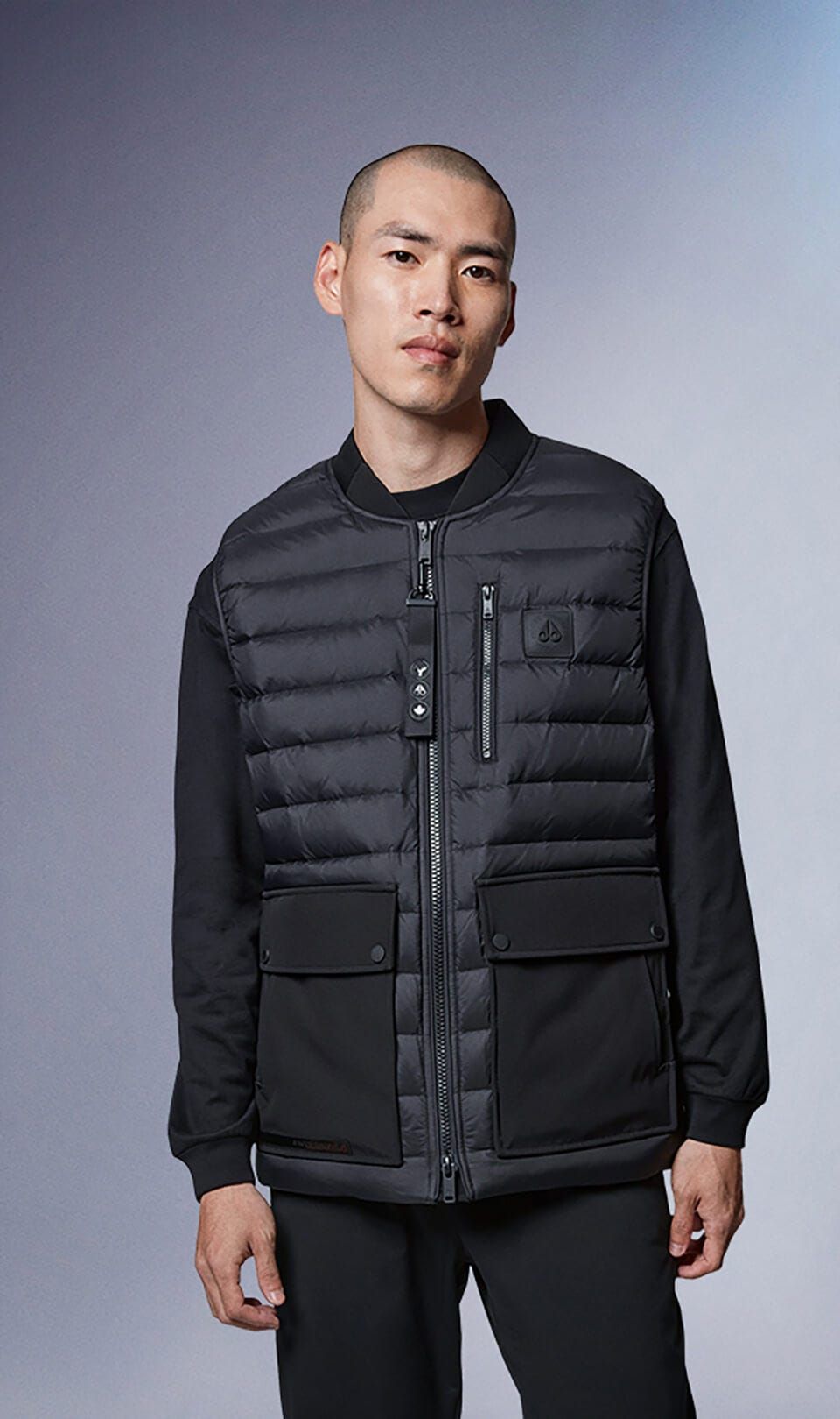 Man wearing a black quilted vest with pockets over a black shirt and black pants.