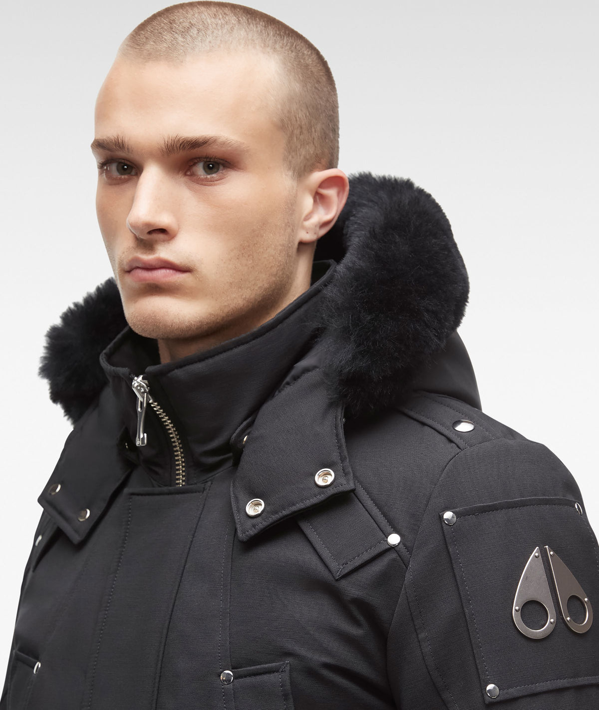 Close-up of a person wearing a black parka with fur trim around the hood and metal accents.