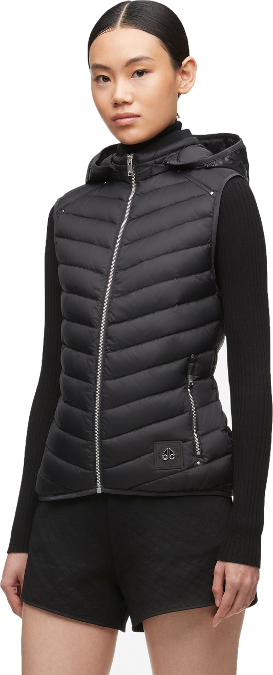A woman wears a quilted black vest with a hood and a black long-sleeved top.