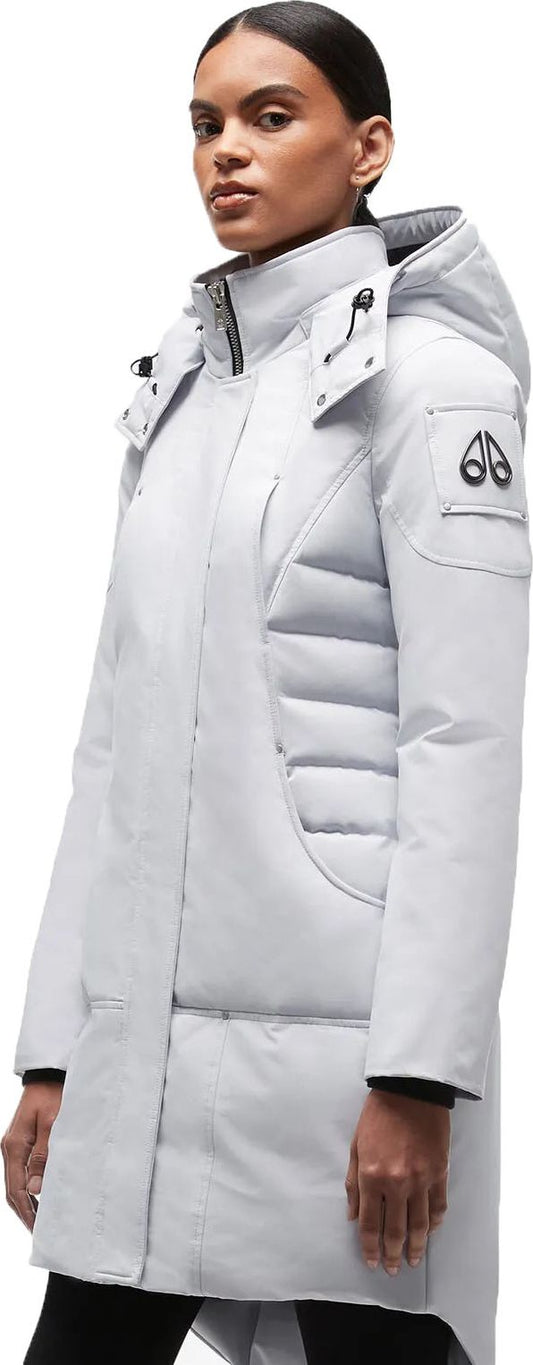 A woman poses in a light gray parka with the moose logo on the sleeve.