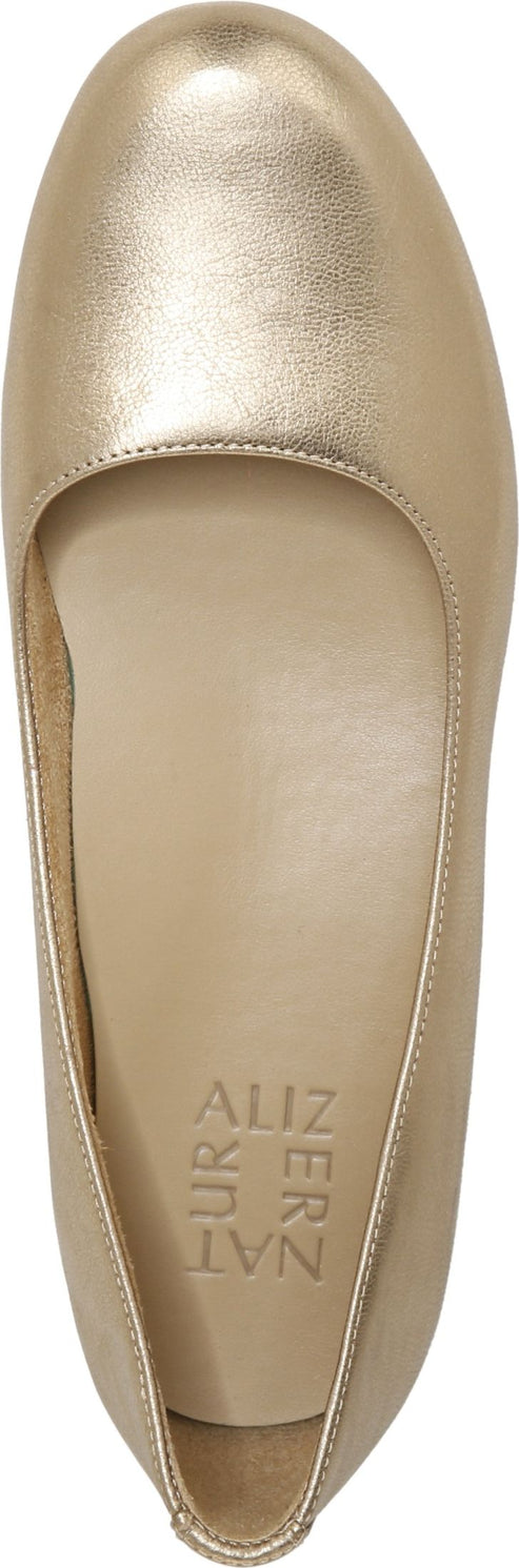 A top-down view of a gold ballet flat, featuring a smooth, rounded toe and the vertically stacked word "NATURALIZER" branded on the insole.