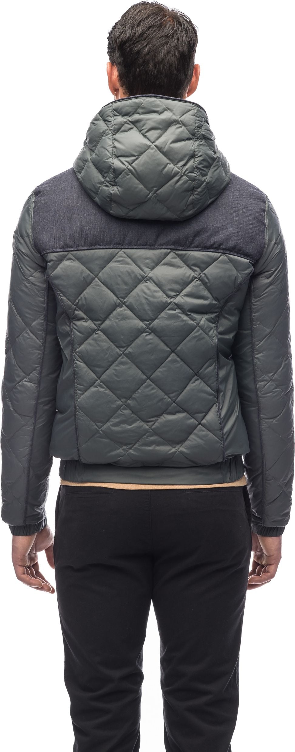 A person wearing a gray, quilted jacket with a hood, with black pants.