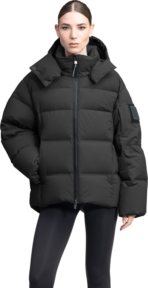A woman in a black puffer jacket with a hood, standing.