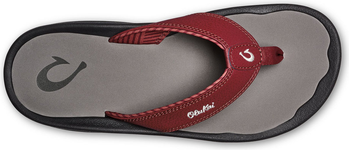 A red and gray sandal with the text 'Olukai' and a hook-like logo.