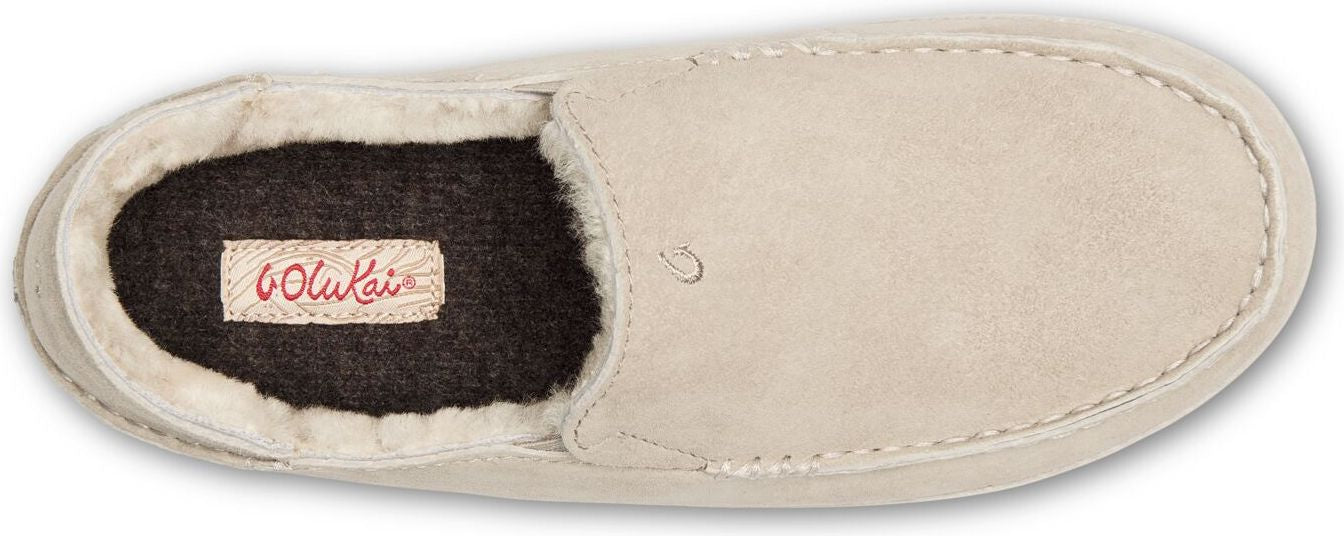 A beige slipper with the brand label 'OluKai' visible on the inner sole.