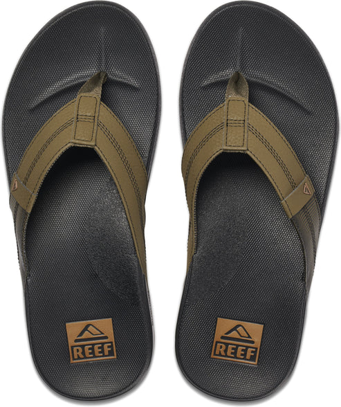 Overhead shot of two black flip flops with khaki straps and a tan rectangle near the heel with a mountain logo that reads "REEF".