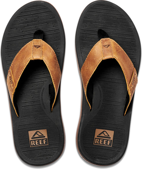 A pair of flip-flops showing a black sole with brown leather straps. The word REEF is displayed in a small box near the heel.