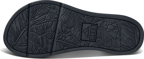 The sole of a dark-colored sandal with a leaf pattern and the word REEF.